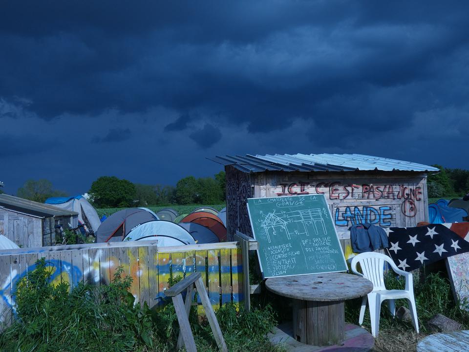 Des cabanes de bois et des tentes à la nuit tombante sur le campement de Zaclay.