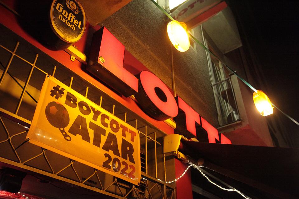 Une affiche boycott Qatar 2022 sur la devanture d'un bar, de nuit sous des lumières rouges 